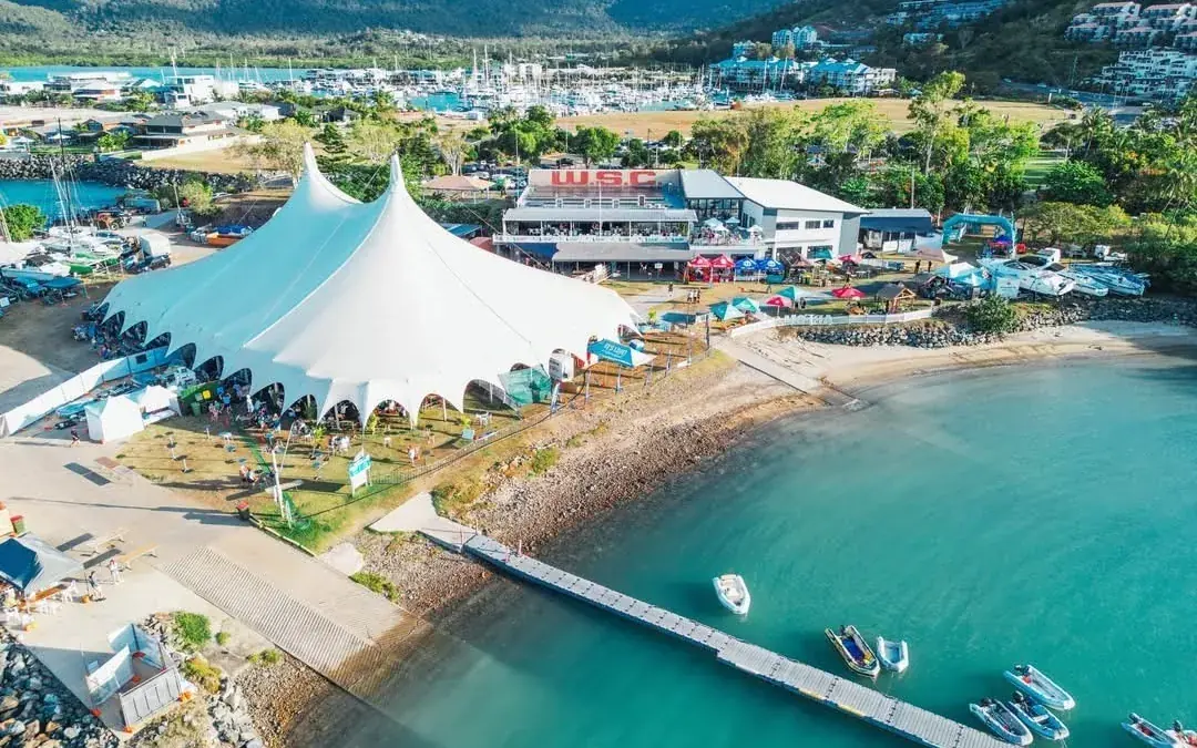 A big top tent on a waterfront festival site beside a marina